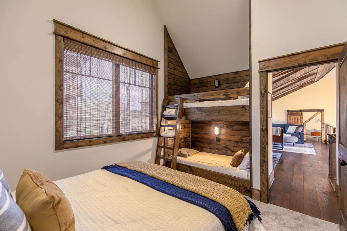 A family-friendly bunk room featuring sturdy bunk beds, a large window for light and nature views, textured bedspreads, and a relaxed, playful atmosphere. The room is designed for fun and togetherness, perfect for kids or group gatherings.