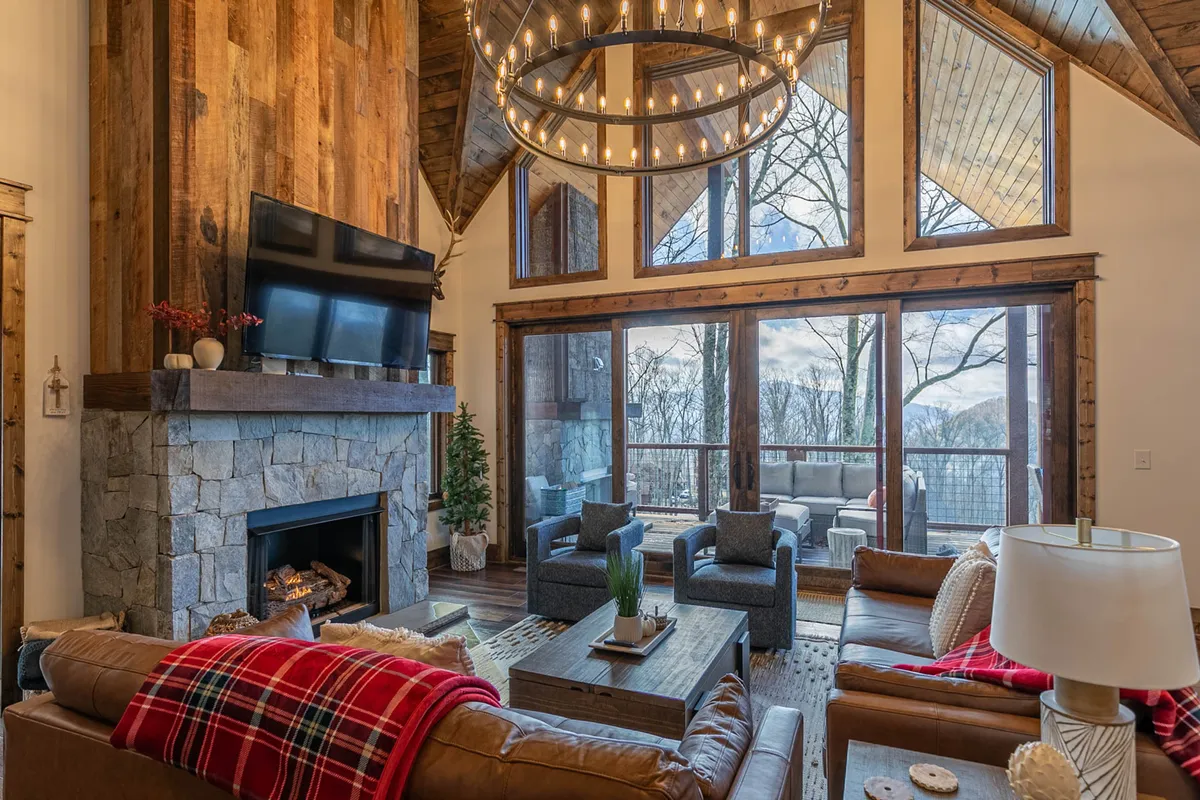 A welcoming interior living area with a prominent fireplace, elegant chandelier, comfortable seating, and large windows framing scenic outdoor views. The space is arranged for relaxation, conversation, and enjoying the sunset.