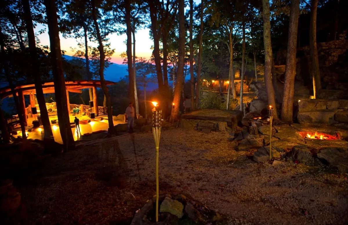 A warm, exterior fire pit seating area flanked by tiki torches and trees, offering a cozy spot for stargazing, sharing s’mores, and intimate conversations. The surrounding landscape enhances the sense of retreat and togetherness.