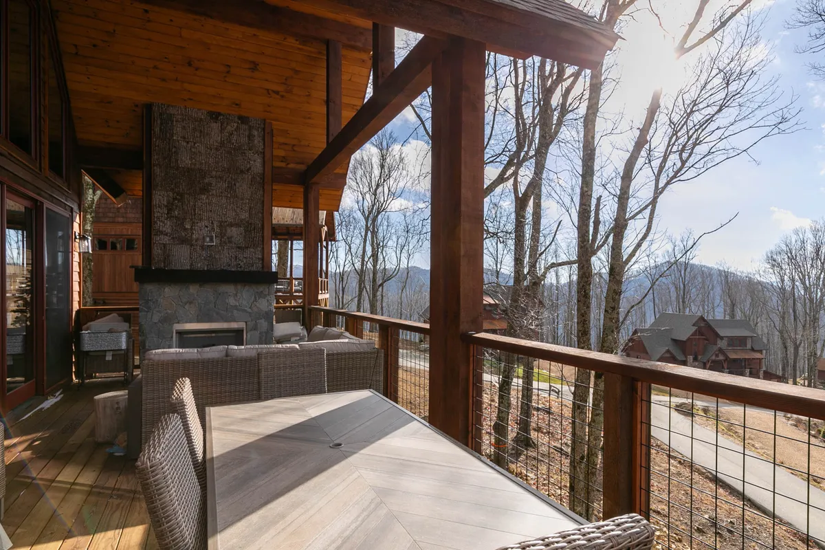 An outdoor seating area with comfortable lounge furniture gathered around a stone fireplace, set against a stunning backdrop of mountain views and trees. The setting is ideal for group meals or evening gatherings, with a cozy yet spacious atmosphere that encourages conversation and relaxation.