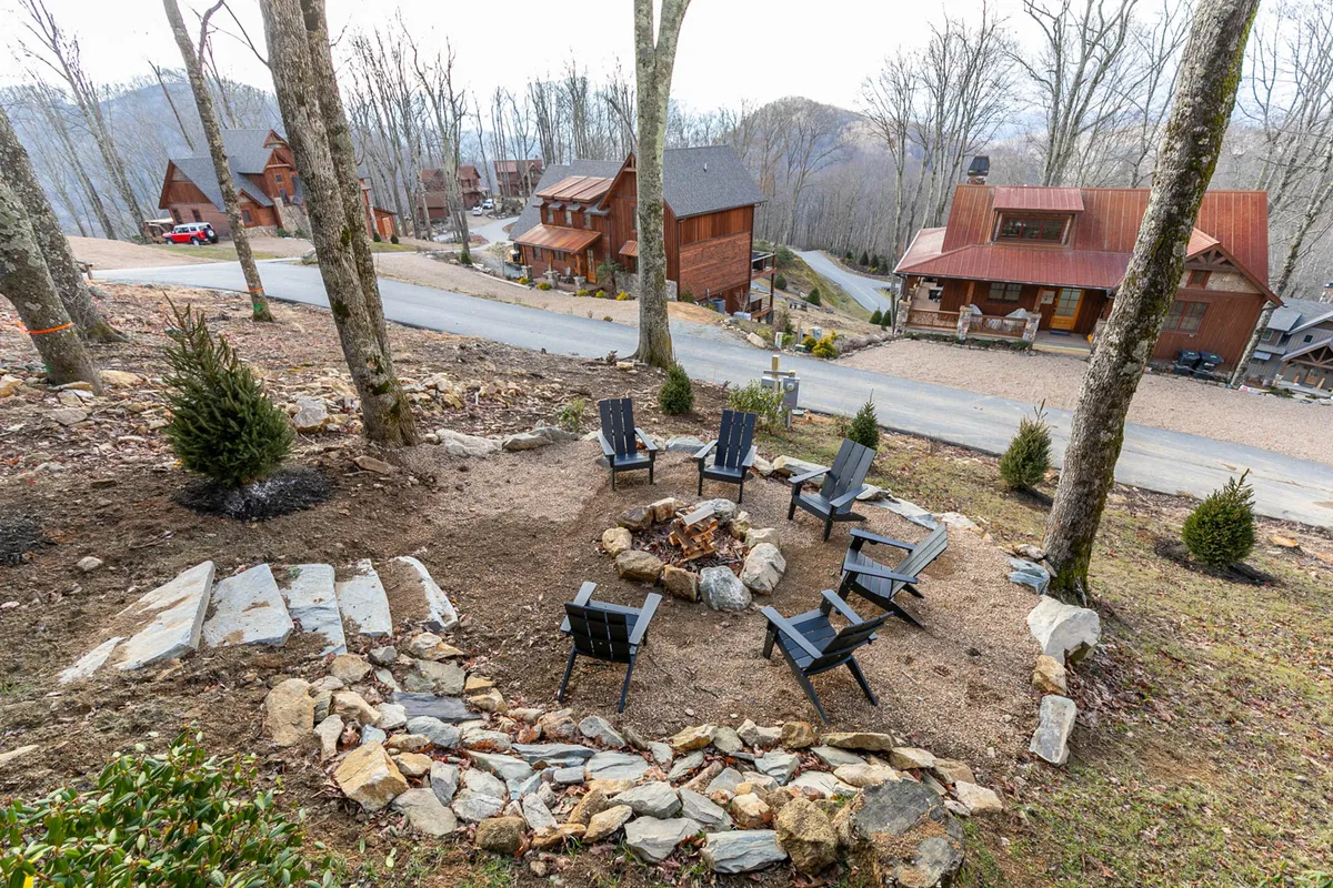 An inviting exterior scene featuring a circular fire pit with surrounding seating nestled among tall trees. Nearby, cozy cabins are visible, contributing to a communal atmosphere ideal for family gatherings and evenings spent outdoors.