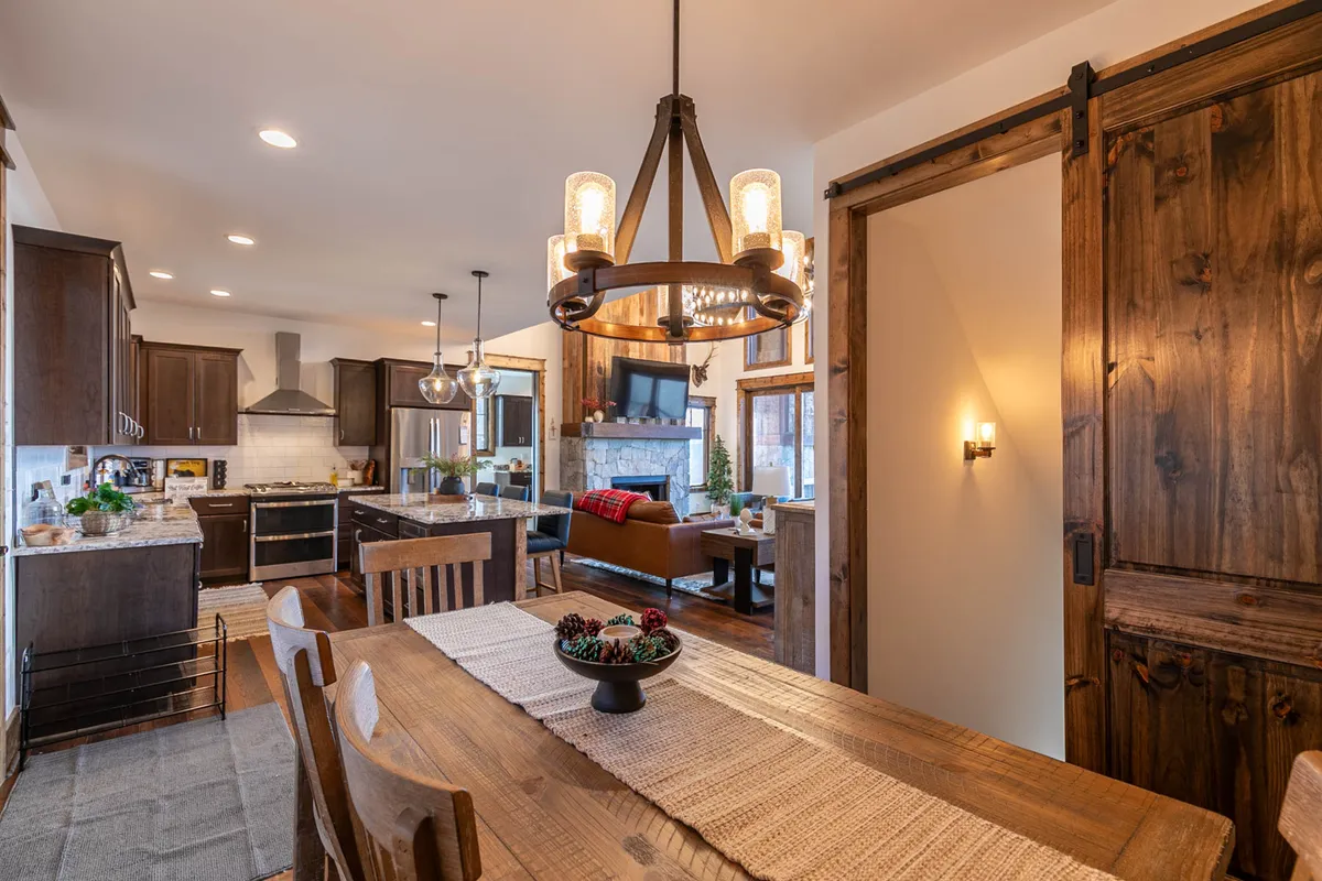 A cozy dining area with a beautifully set wooden table, a stylish chandelier overhead, and the kitchen island visible in the background. The decor suggests intimate, festive family meals and holiday celebrations.