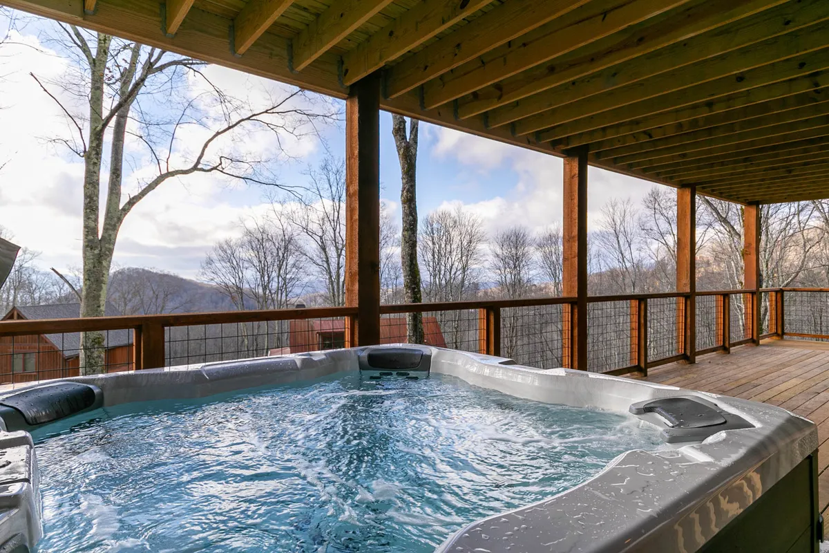 A luxurious hot tub is nestled on a deck with panoramic mountain views and surrounded by lush trees. The scene suggests both relaxation and shared enjoyment, perfect for unwinding between group activities or evenings after a day of adventure.