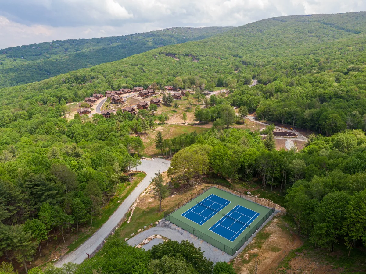 An inviting view of the tennis courts nestled among lush greenery with the mountains and residential spaces as a backdrop. The scene suggests active recreation and opportunities for community bonding, with well-maintained facilities and an open, welcoming environment.