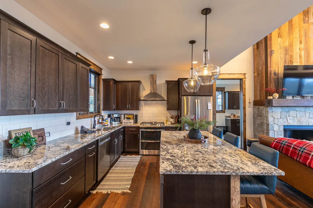 A chef-inspired kitchen featuring a granite countertop island, high-end stainless steel appliances, warm wood cabinetry, and pendant lighting. The kitchen is open, inviting, and set up for both cooking and entertaining, with seating that invites conversation.